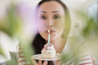 Woman blowing out birthday candle on cupcake