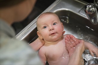 Caucasian mother bathing baby in sink