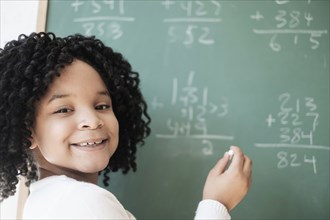 African American student writing on chalkboard in classroom