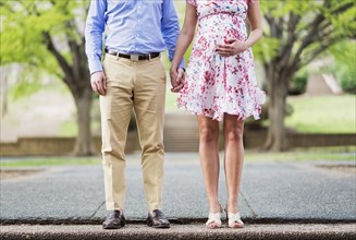 Pregnant Caucasian couple holding hands outdoors