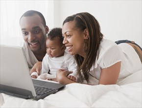 African couple and baby using laptop on bed