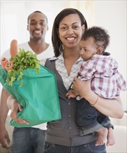 African couple holding baby and groceries in reusable bag