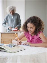 Girl doing homework with grandmother in background
