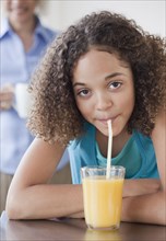 Mixed race girl drinking orange juice with straw