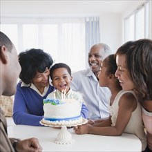 African American family watching grandson blow out birthday candles