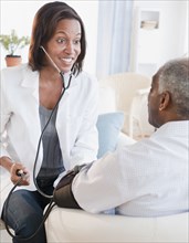 Black doctor checking senior man's blood pressure