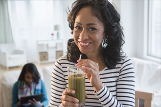 Mother drinking green smoothie while daughter uses digital tablet