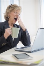 Fatigued Caucasian businesswoman drinking coffee and yawning