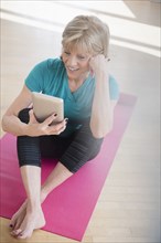 Older Caucasian woman on exercise mat using digital tablet