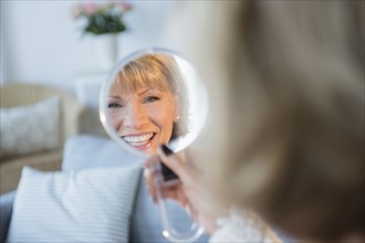 Older Caucasian woman smiling in handheld mirror