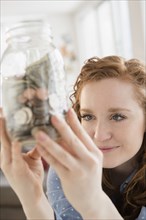 Caucasian woman looking at money in savings jar