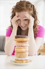 Caucasian woman resisting pile of donuts on plate