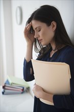 Caucasian businesswoman with headache holding file folder in office