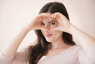Caucasian woman gesturing heart-shape with hands over eyes