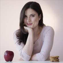 Caucasian woman choosing between apple or cookies for snack