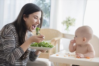Caucasian woman eating salad while watching baby daughter