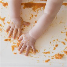 hands of Caucasian baby girl self-feeding mashed sweet potato