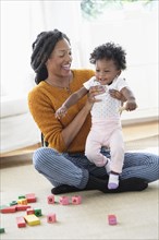 Black mother and baby daughter playing with blocks on carpet