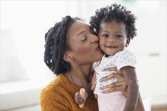 Smiling Black mother kissing baby daughter on cheek