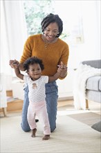 Black mother helping baby daughter learn walking
