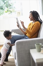 Black woman using digital tablet on sofa near baby daughter
