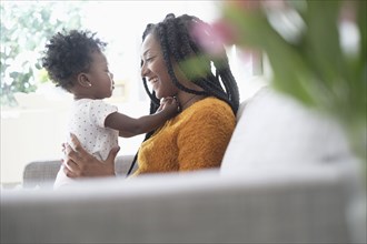 Black woman playing with baby daughter on sofa
