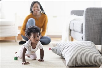 Black woman watching baby daughter crawl toward pillow