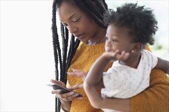 Black woman holding baby daughter using cell phone