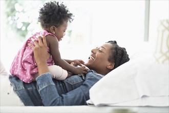 Black woman playing with baby daughter on bed