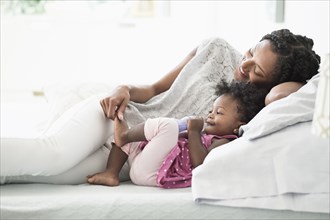 Black woman playing with foot of baby daughter on bed