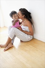 Black woman sitting on floor kissing cheek of baby daughter