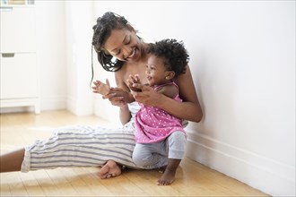 Black woman sitting on floor kissing clapping hands with baby daughter