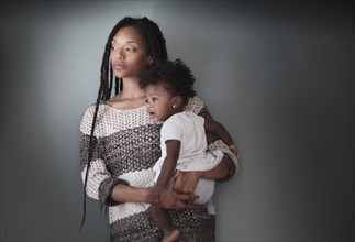 Thoughtful Black woman standing holding baby daughter