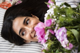 Indian woman laying on bed holding bouquet of flowers