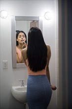 Indian woman applying lipstick in bathroom mirror