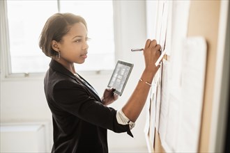 Black businesswoman using digital tablet writing on paperwork