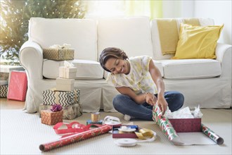 Black woman sitting on floor wrapping gifts