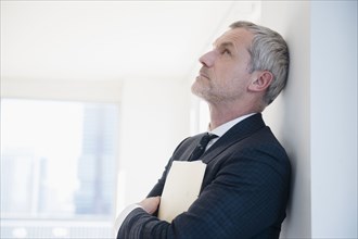 Older frustrated Caucasian businessman leaning on wall