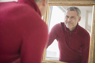 Older Caucasian man wearing sweater smiling in mirror