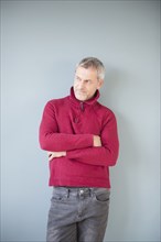 Older Caucasian man wearing sweater leaning on wall