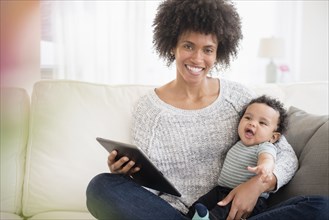Mother sitting on sofa holding baby son and digital tablet
