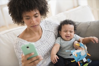 Mother holding crying baby son while texting on cell phone