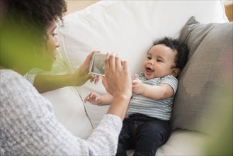 Mother photographing baby son with cell phone on sofa