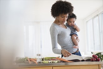 Mother reading cookbook while holding baby son