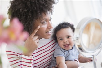 Mother holding baby son applying face cream in mirror