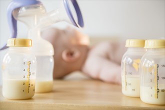 Caucasian baby boy laying near bottles of breast milk and breast pump