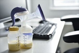 Breast pump and bottle of breast milk near computer