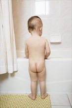 Naked Caucasian baby girl standing at bathtub