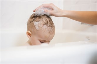 Caucasian mother washing hair of baby daughter in bathtub