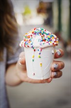 Caucasian woman holding cup of melting ice cream with sprinkles